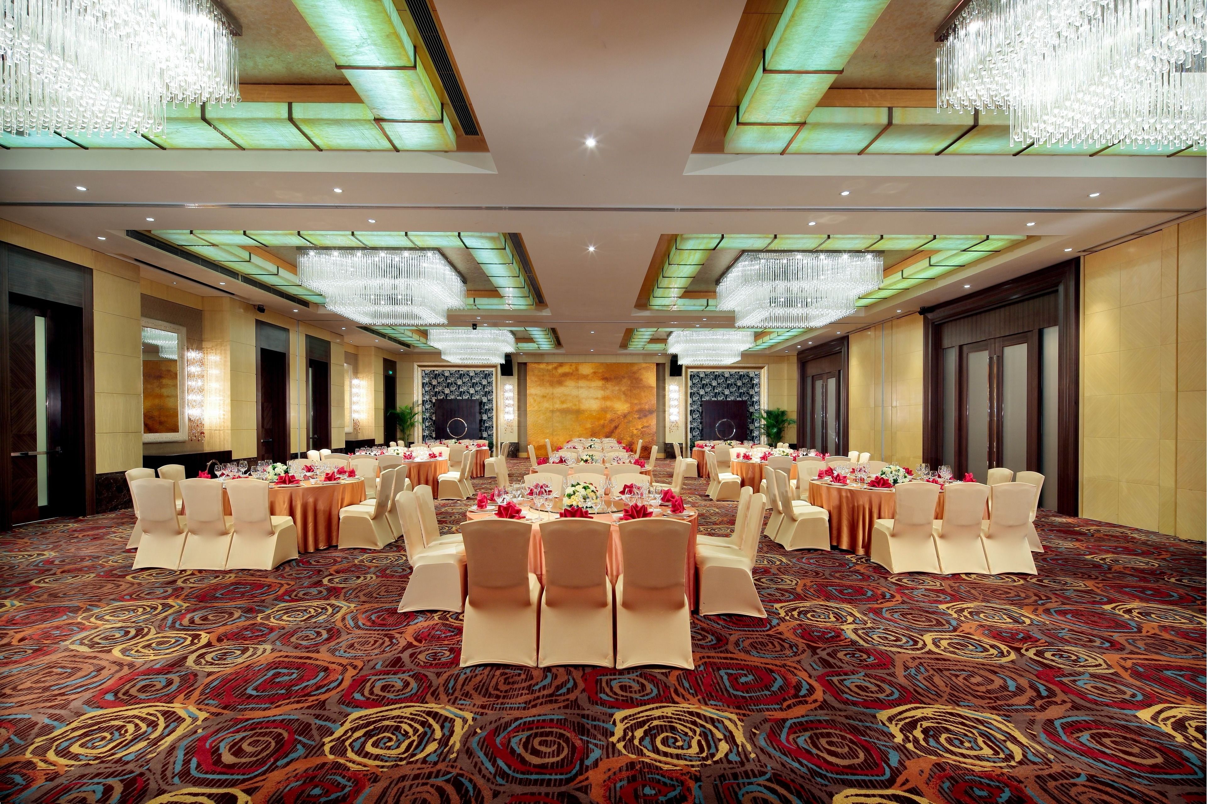 A banquet hall with round tables, white chairs, and chandeliers.