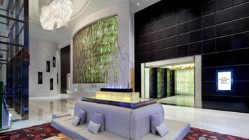 A modern lobby with a seating area, a decorative wall, and a large chandelier.