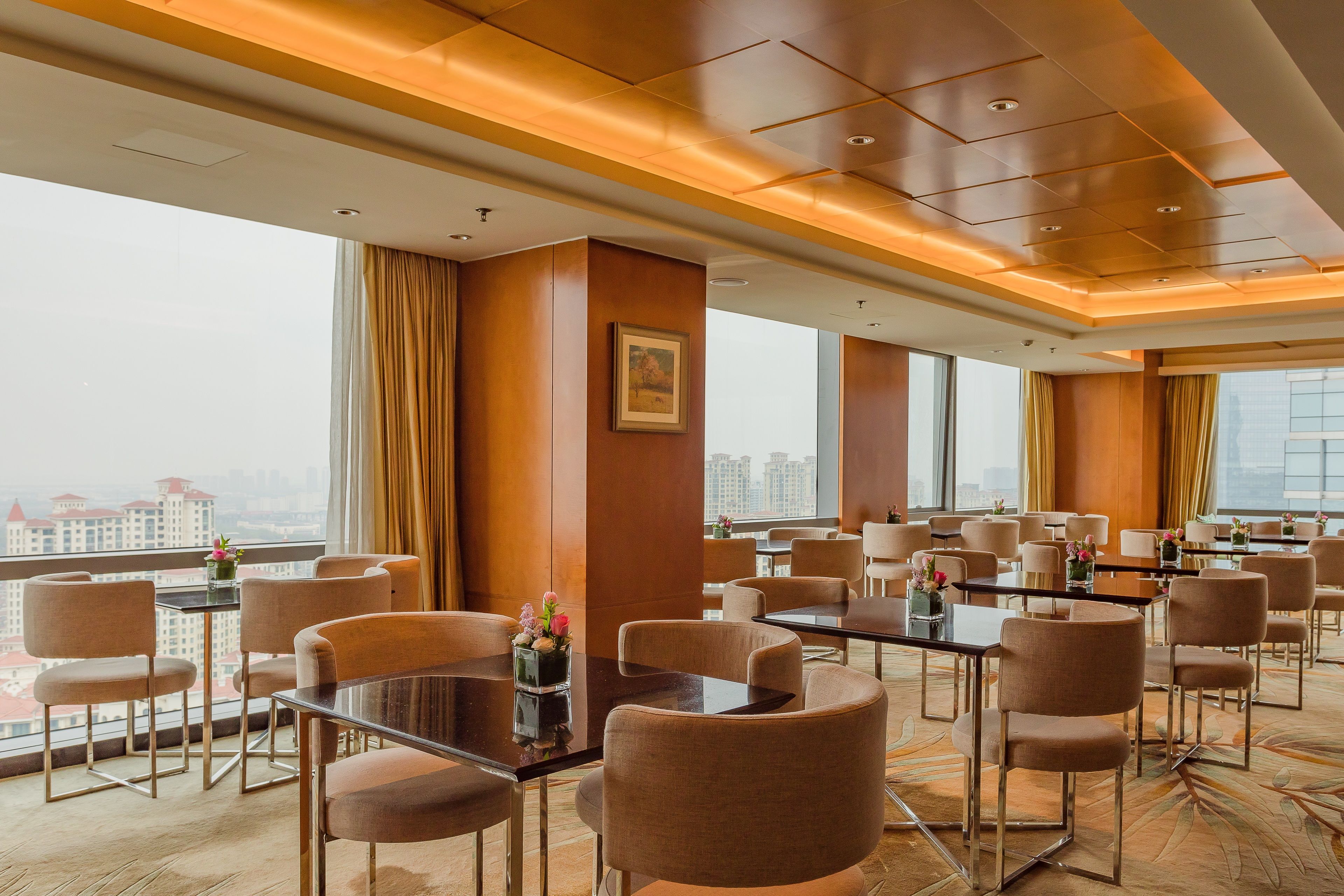 Un salón de conferencias de hotel con mesas y sillas, ventanas amplias y vistas a la ciudad.