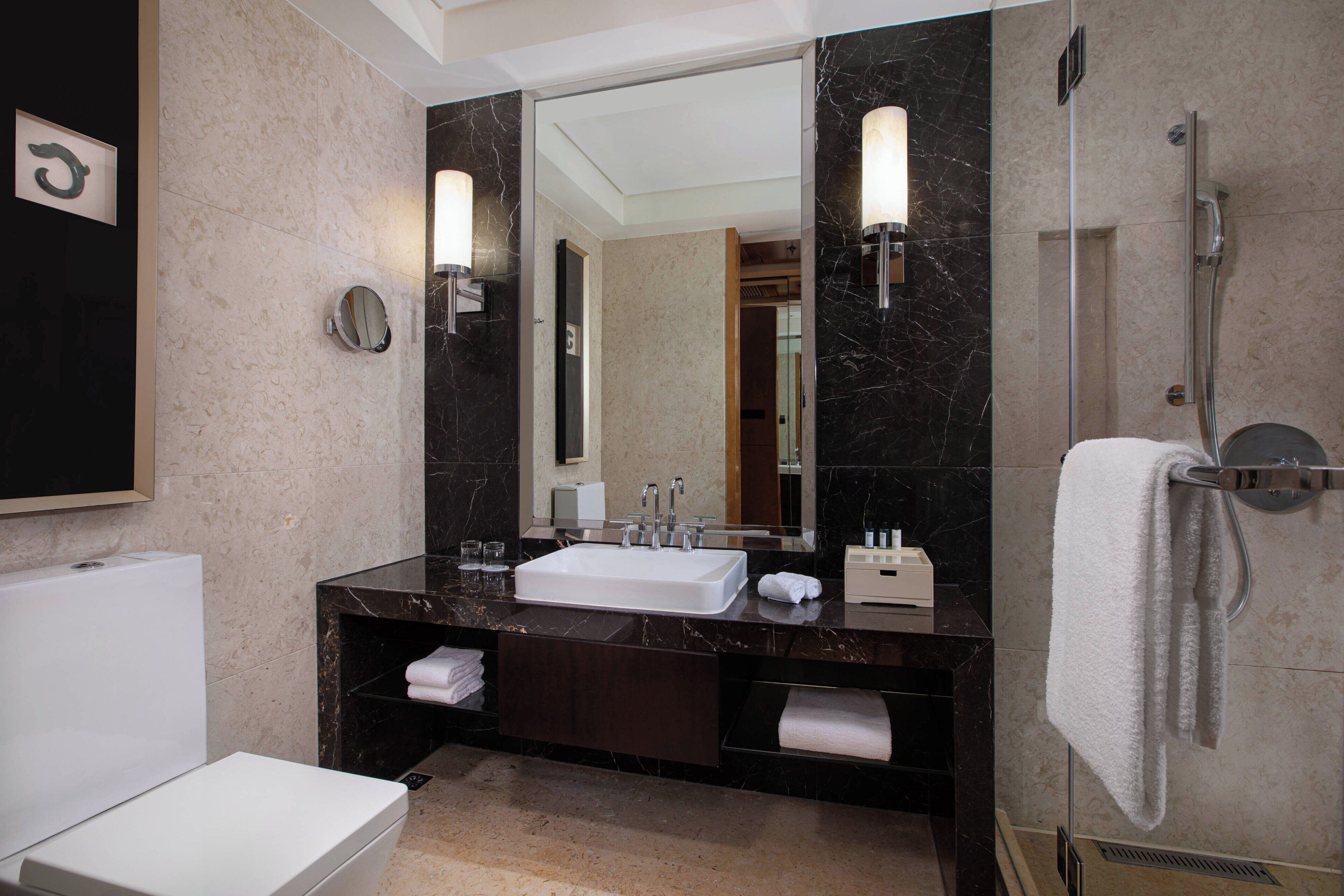 A modern bathroom with a white sink, dark marble countertop, and a large mirror.