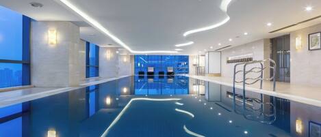 A modern indoor swimming pool with a clear view of the cityscape through large windows.