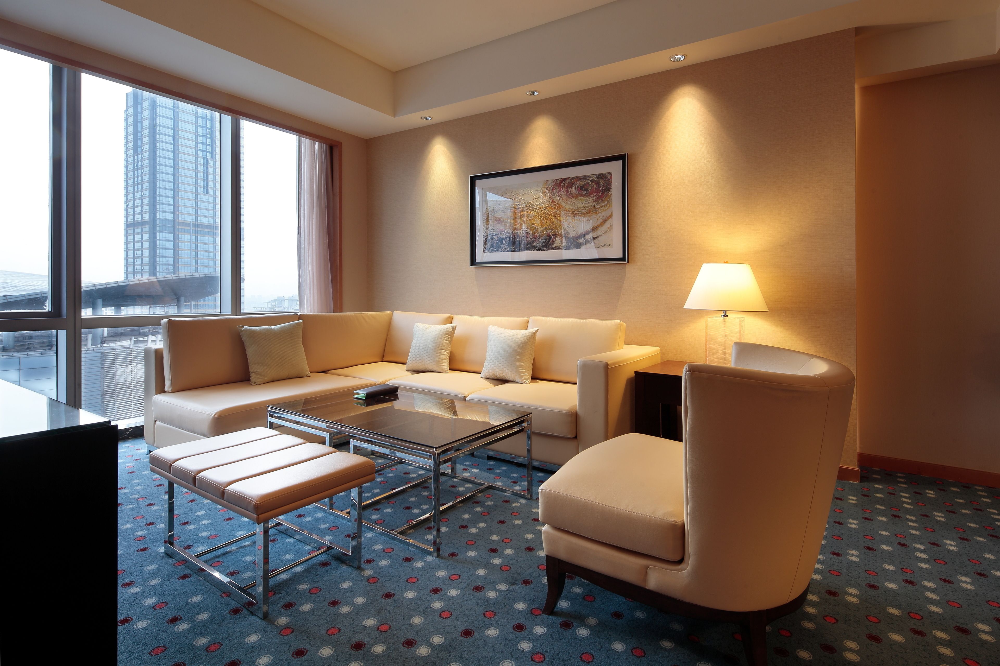Una habitación de hotel moderna con un ventanal grande, un sofá, una mesa de centro y una silla.