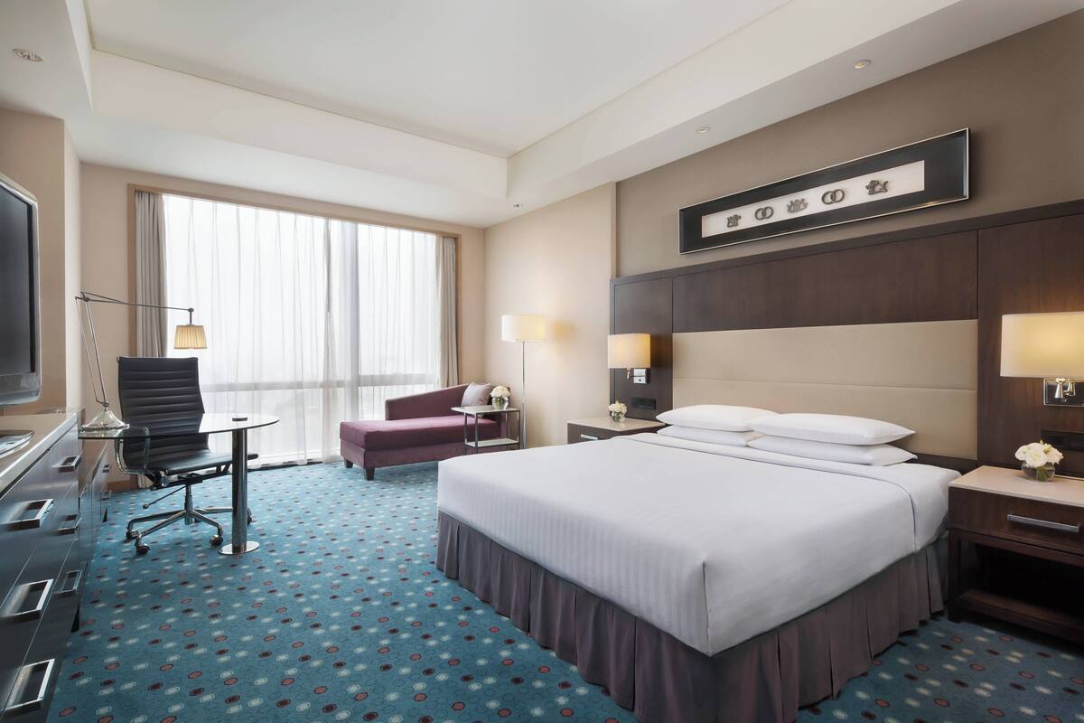 Una habitación de hotel con una cama grande, un escritorio con silla, un televisor y una ventana con cortinas.