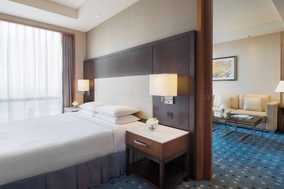 Una habitación de hotel con una cama grande, dos mesitas de noche con lámparas, un tocador, un sofá y una alfombra estampada.