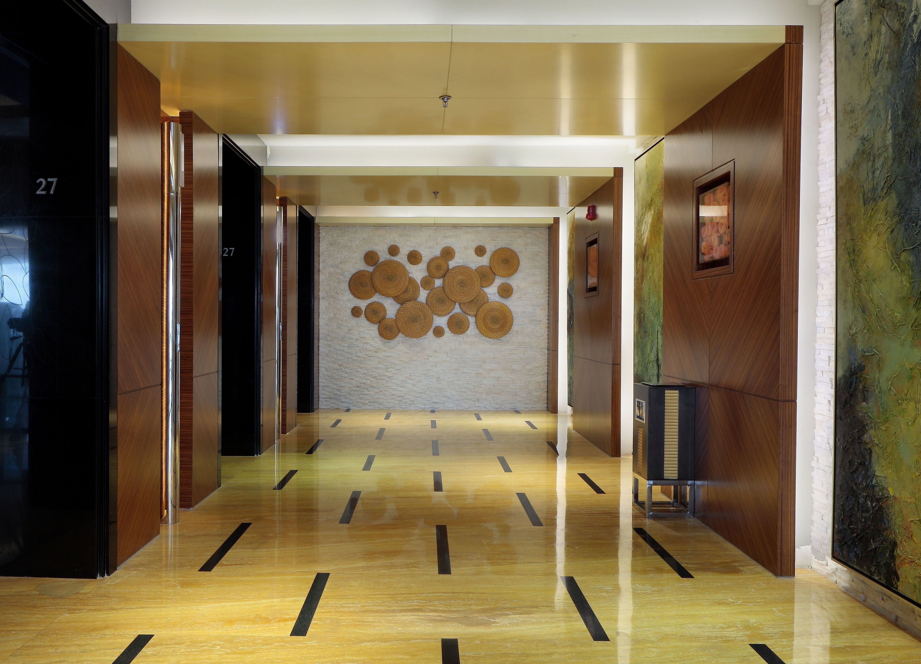 A modern hallway with a wooden floor, a wall with circular wall art, and a large abstract painting on the right.