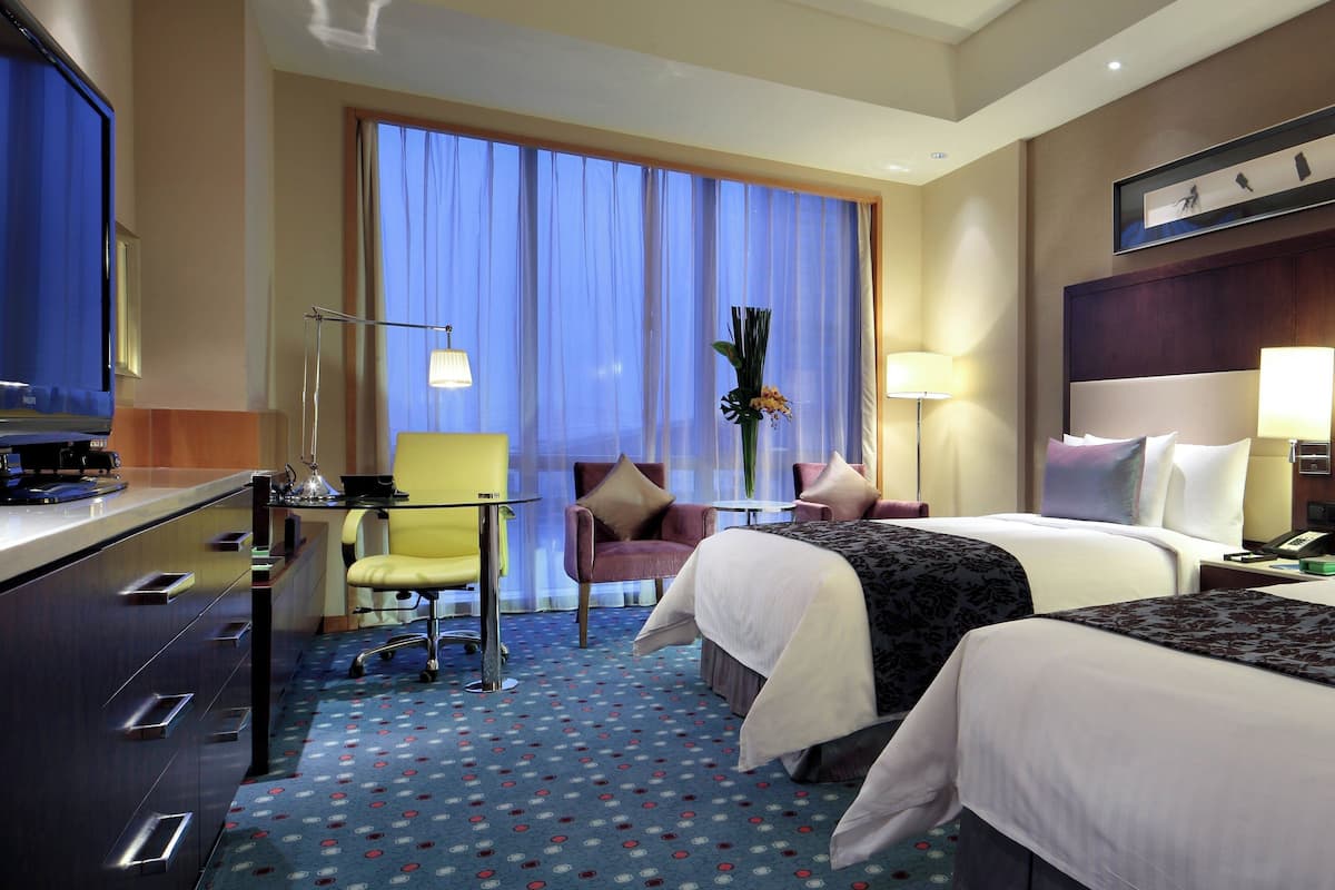 Habitación de hotel con cama, escritorio, silla y ventana grande con cortinas.