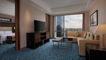 A hotel room with a bed, a TV, a sofa, a coffee table, and a large window with a city view.