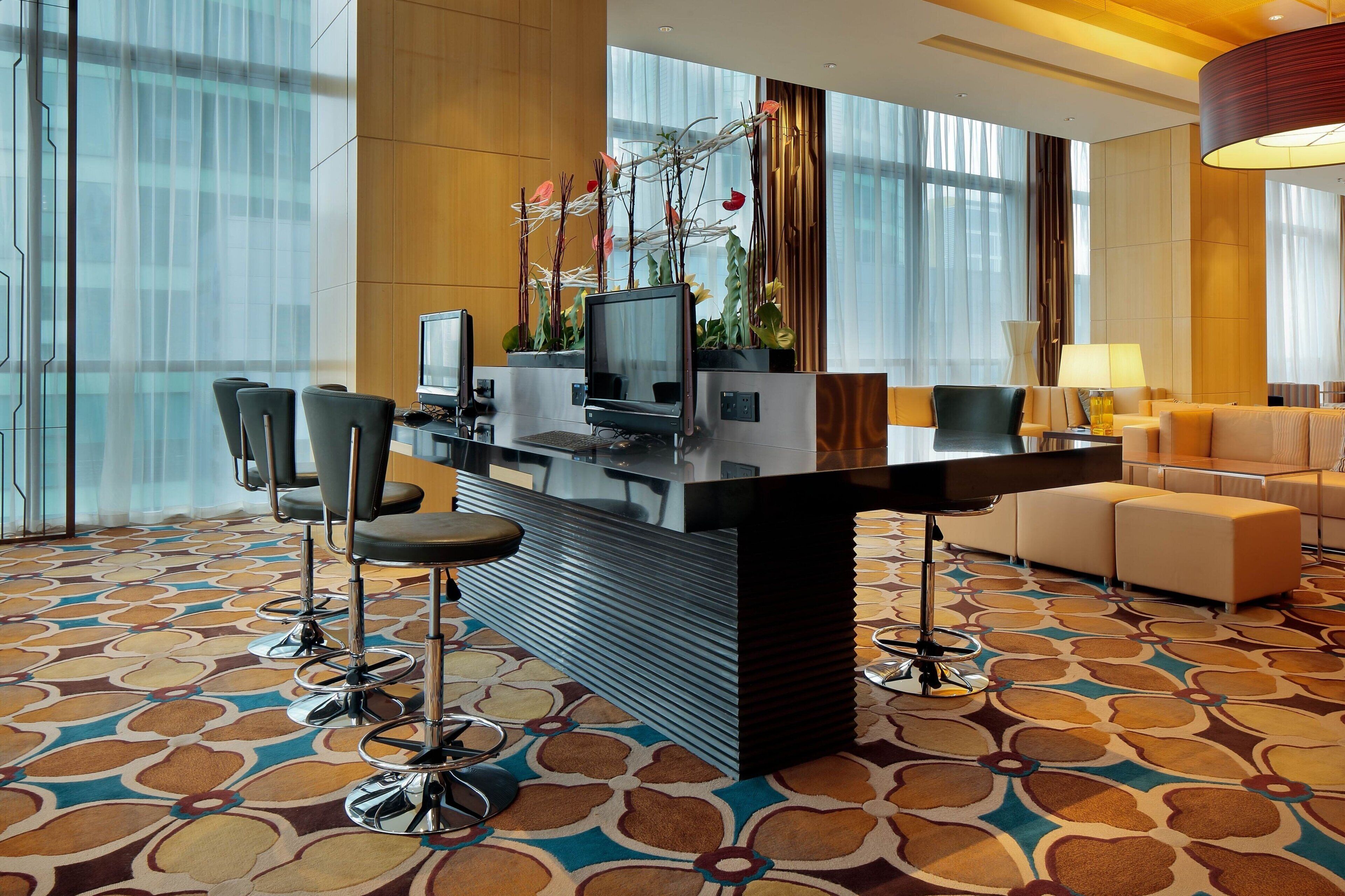 A hotel lobby with a reception desk, bar stools, a sofa, and a patterned carpet.