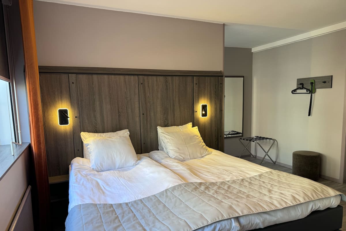 A modern bedroom with a large bed, two bedside tables, a wooden headboard, and a wall-mounted mirror.