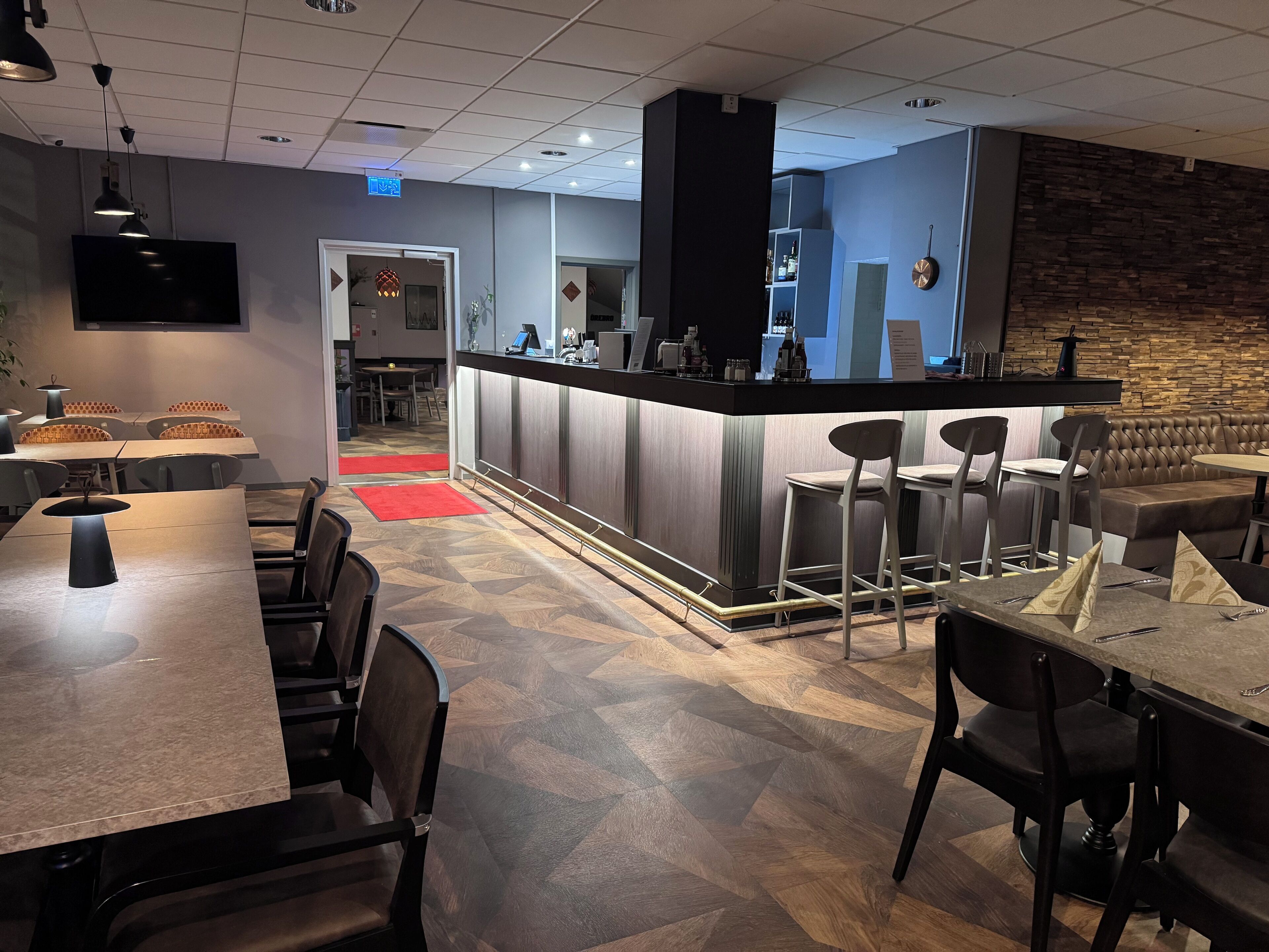 Um restaurante moderno com área de bar, cadeiras altas e piso em padrão herringbone.