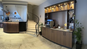 A hotel reception area with a wooden reception desk, a digital screen, and a staircase.