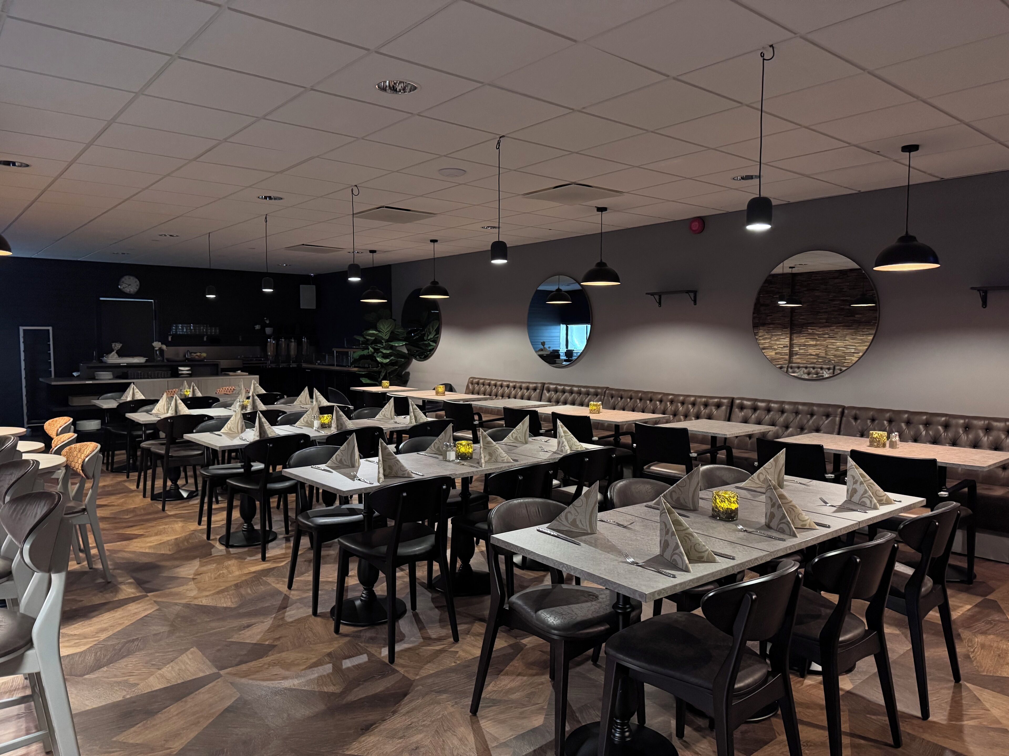 A restaurant with multiple tables and booths, a bar area, and a large mirror on the wall.