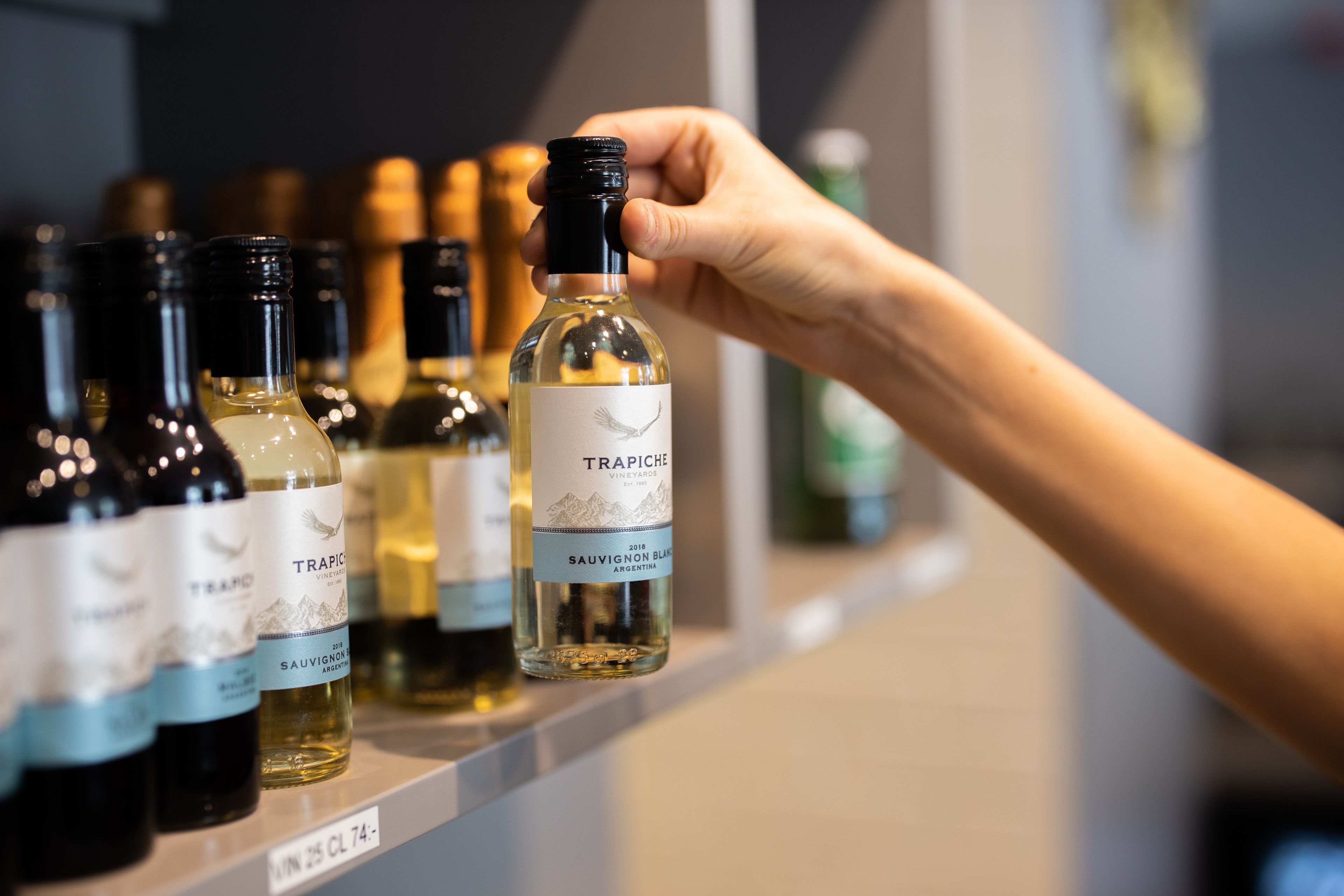 En hand håller i en vinflaska med en etikett som visar texten: ”TRAPICHE SAUVIGNON BLANC ARGENTINA”.