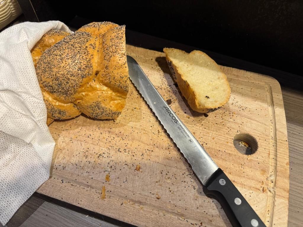 A loaf of poppy seed bread on a wooden cutting board with a knife.