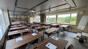 A classroom with wooden desks and chairs, large windows, and a projector on the ceiling.