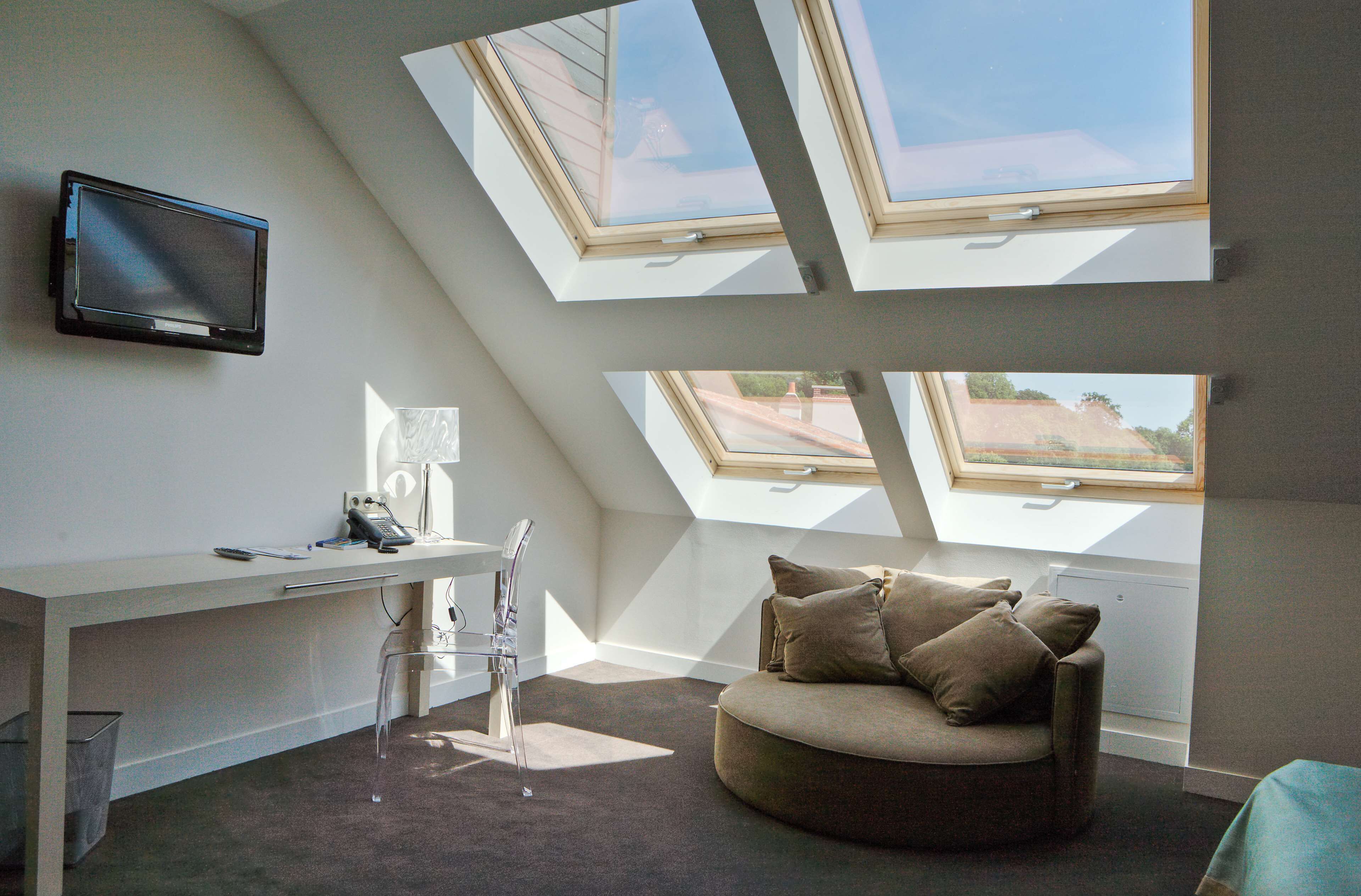 Een moderne kamer met een bureau, een transparante stoel, een bank en dakramen.