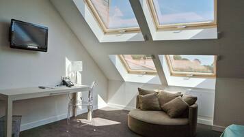 Een moderne kamer met een bureau, een transparante stoel, een bank en dakramen.