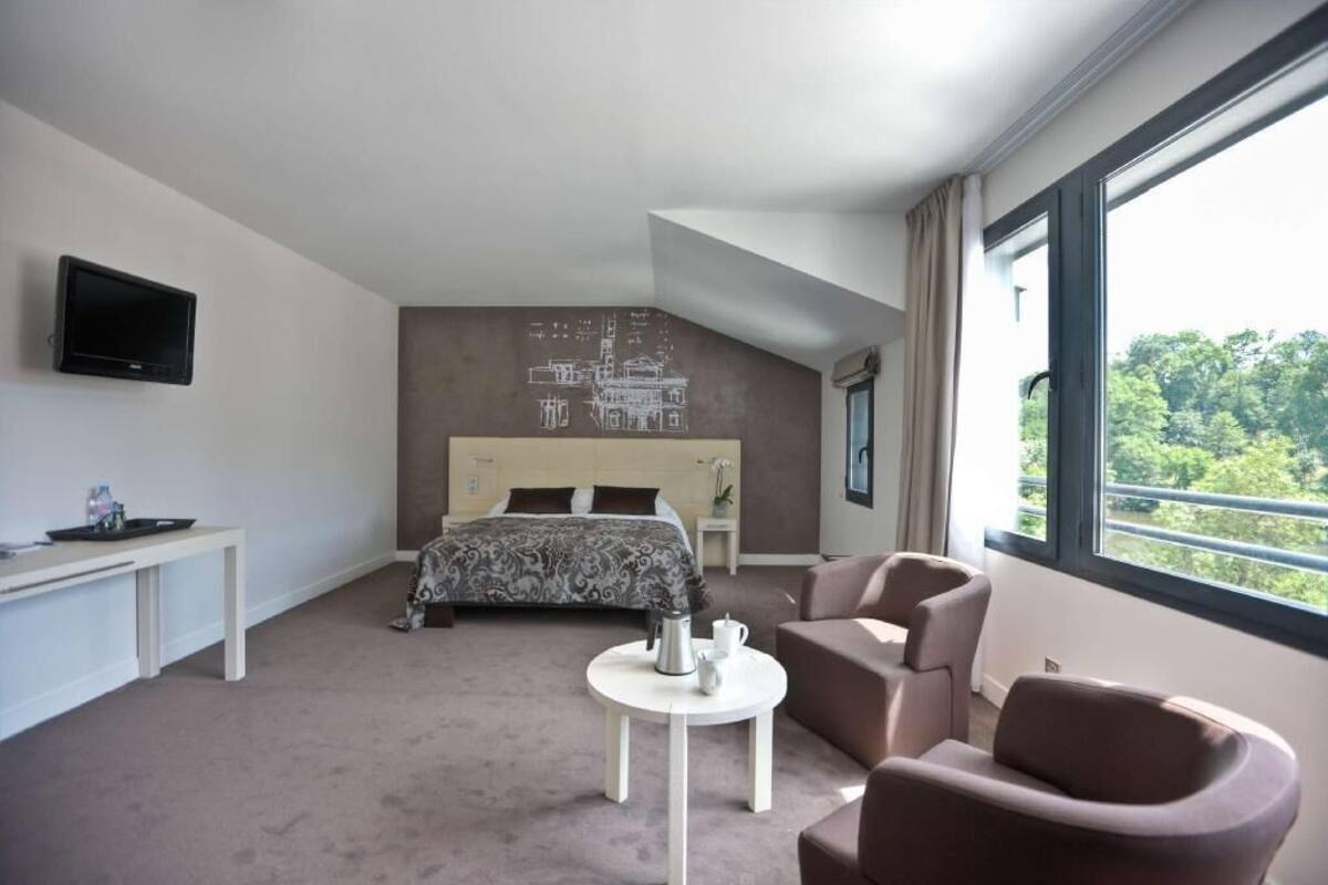 Habitación de hotel moderna con una cama, un escritorio, una silla, una mesita y un televisor.