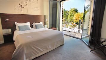 Una habitación de hotel con una cama grande, cabecera de madera, puerta de vidrio que da a un balcón exterior y una pared con detalles decorativos escritos.