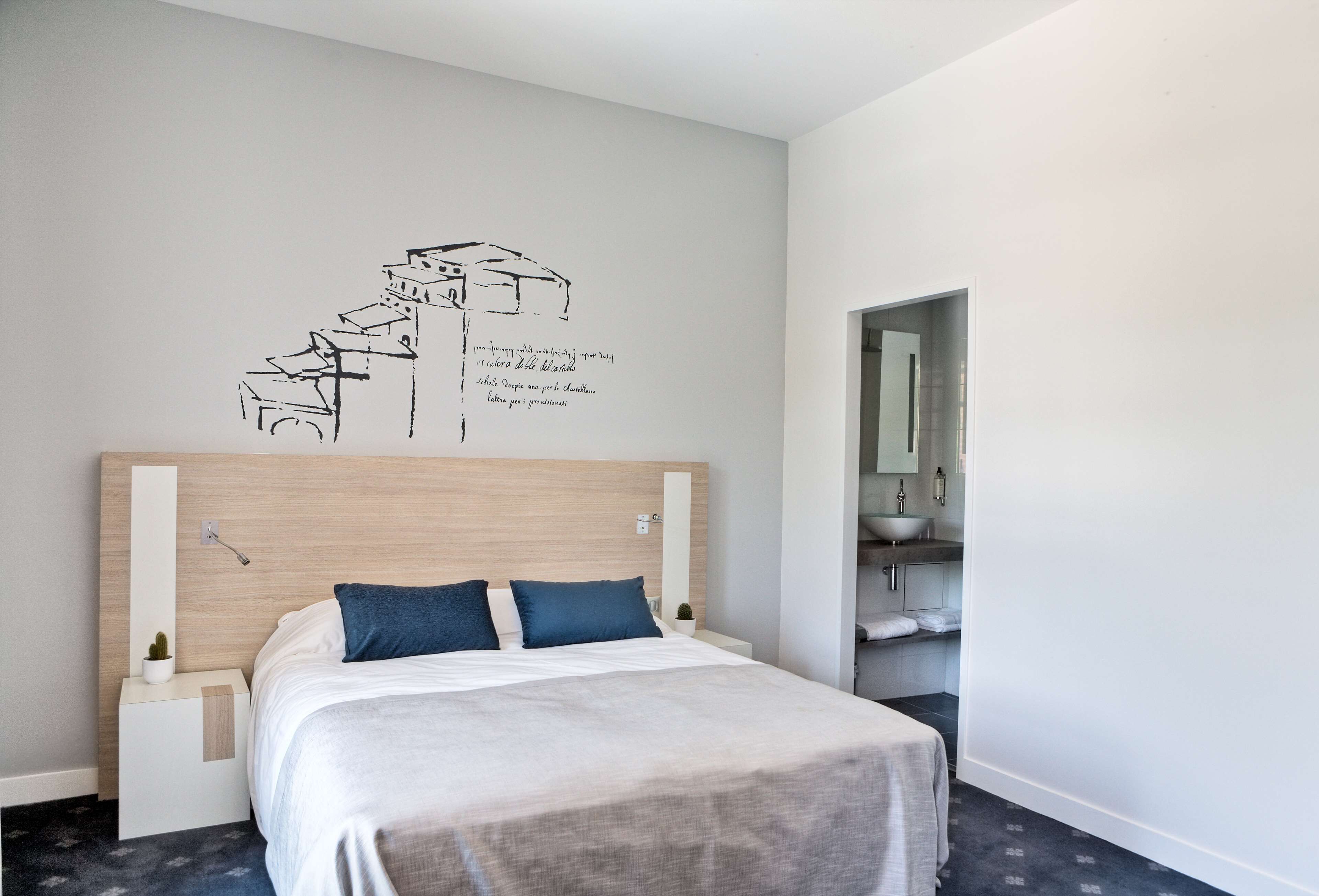 Une chambre d’hôtel avec un lit, une décoration murale représentant des bâtiments, une petite plante et une table de chevet.