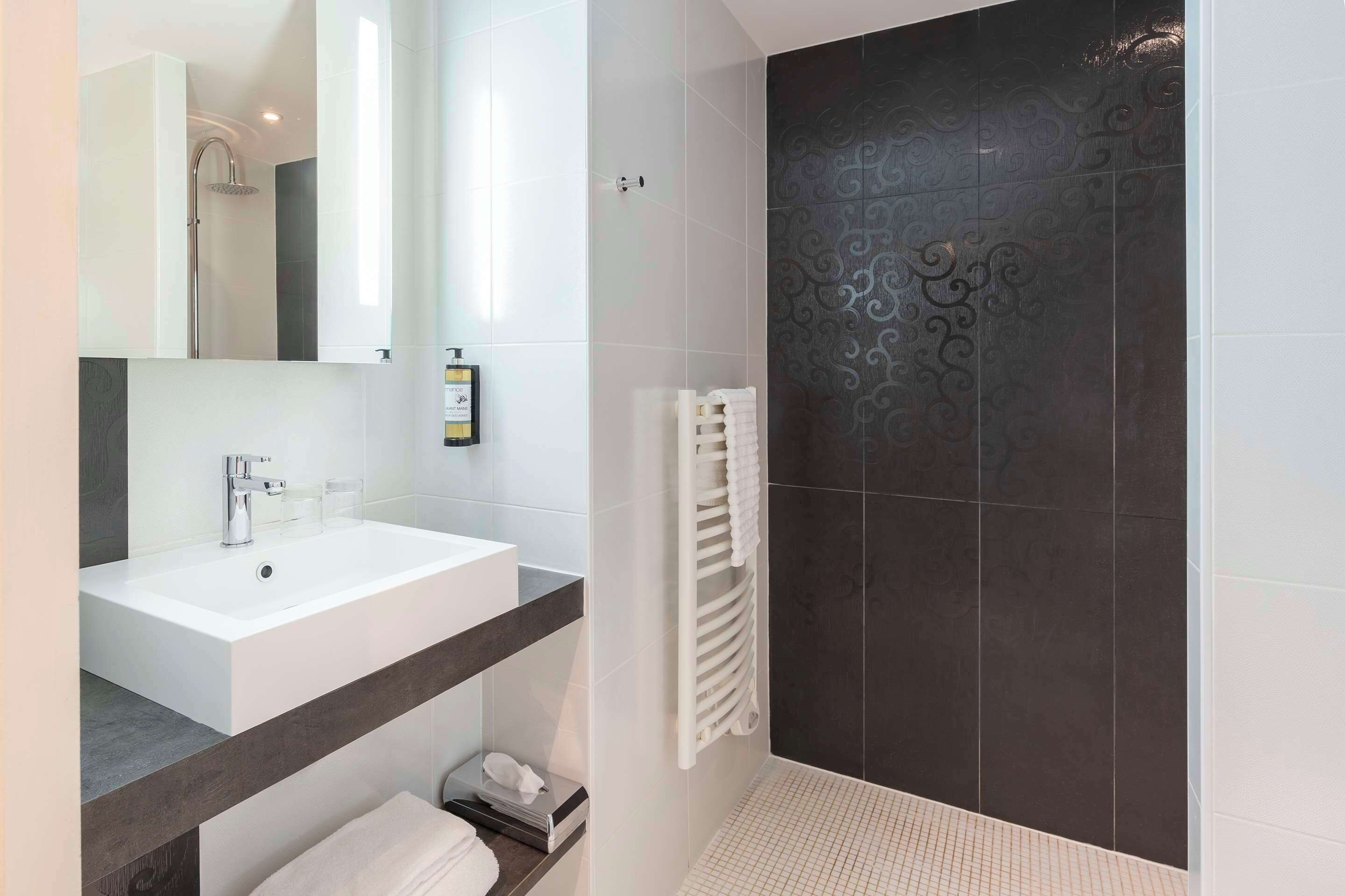 Un baño moderno con un lavamanos blanco, un espejo grande y una zona de ducha con azulejos oscuros.