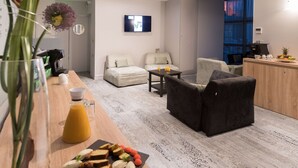 Un salon moderne avec un canapé, une table basse et un coin repas où l’on peut prendre le petit-déjeuner, avec des toasts et des fruits.