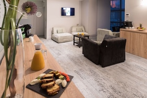 Uma sala de estar moderna com sofá, mesa de centro e um espaço para café da manhã com torradas e frutas.