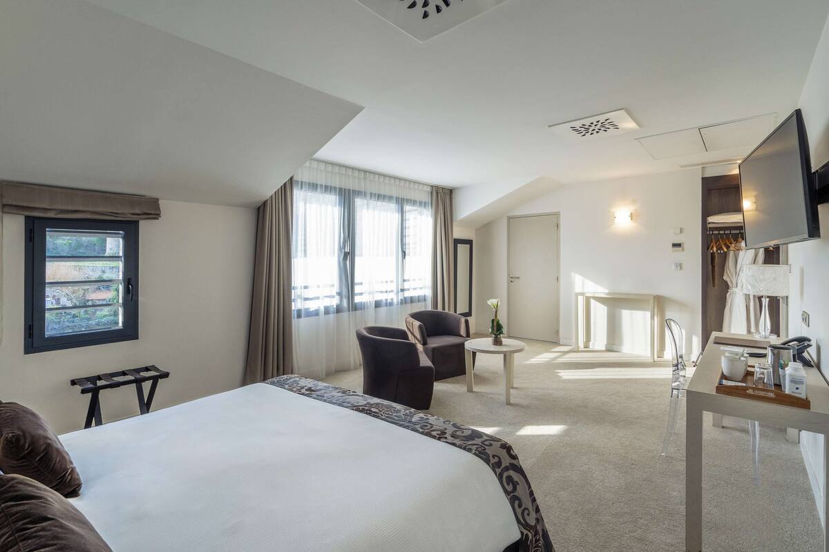 Una habitación de hotel con una cama grande, un escritorio con silla, una mesita pequeña y un televisor.