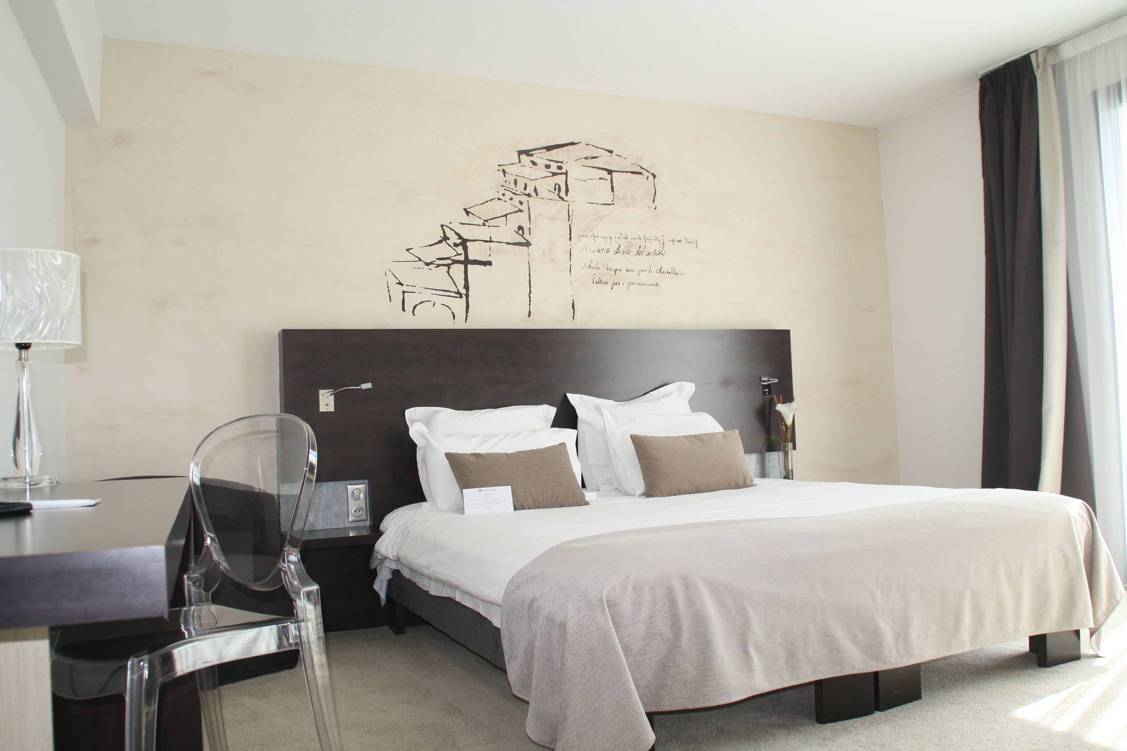 A hotel room with a large bed, a desk with a chair, and a wall art piece.