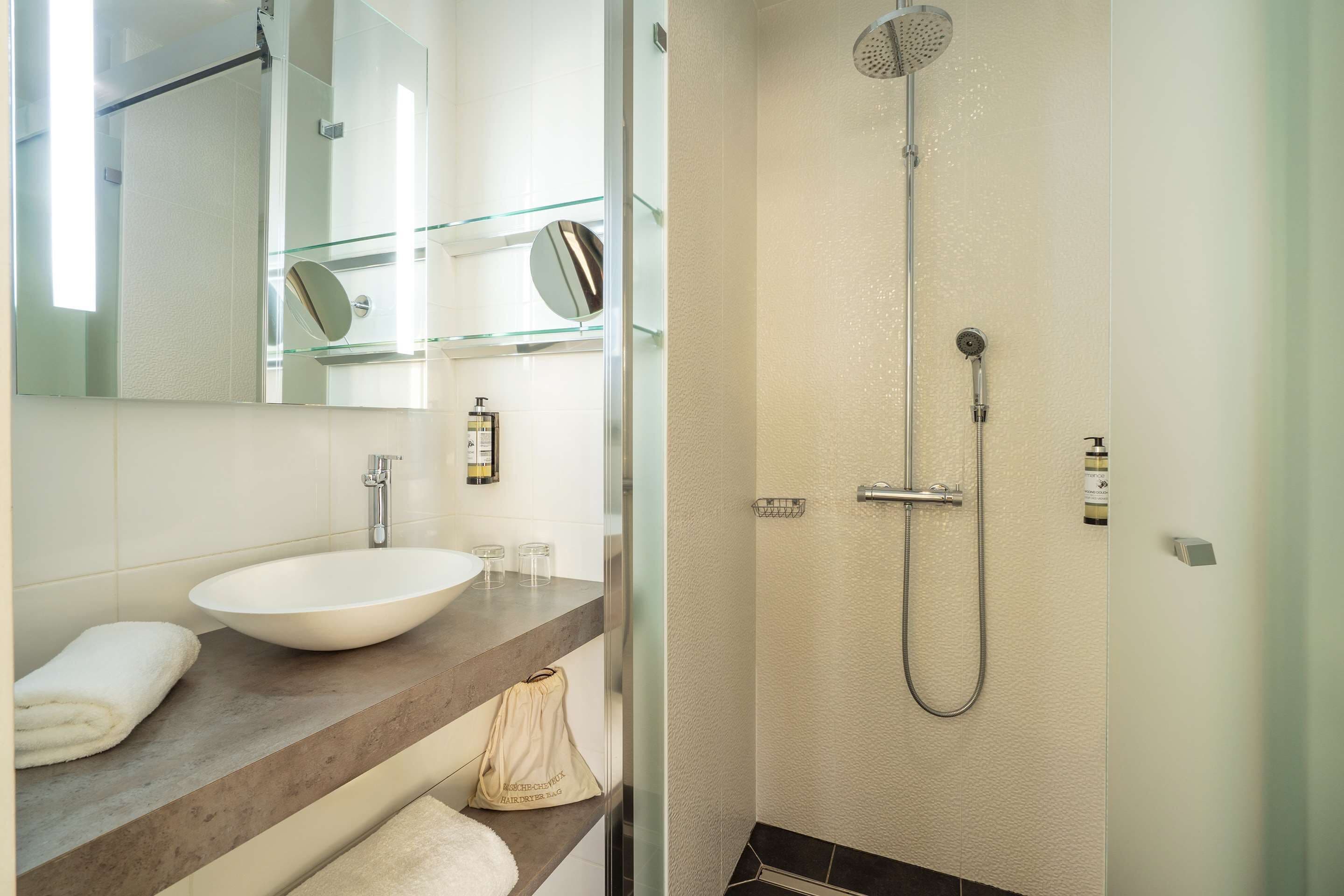 A bathroom with a large white sink, a glass shower enclosure, and a mirror above the sink.