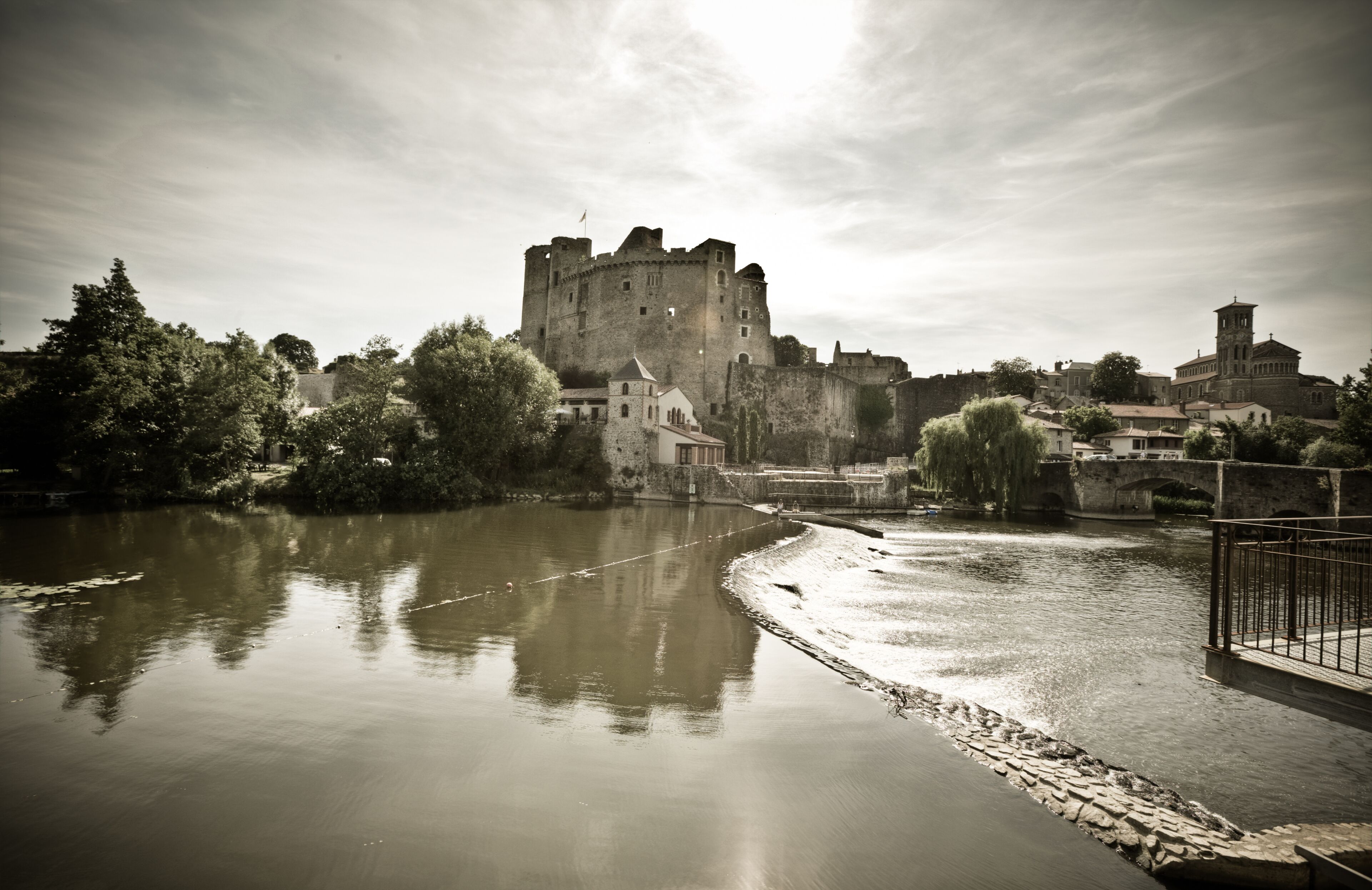Un castillo histórico rodeado por un río, con edificios de piedra y un puente cercano.