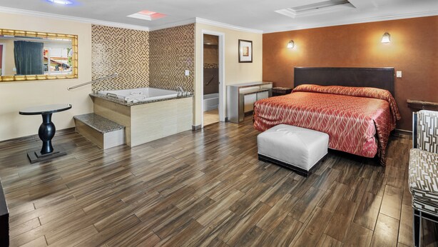 A hotel room with a large bed, a small sitting area, a bathtub, and a separate shower area. - Sky Palm Motel (Orange)