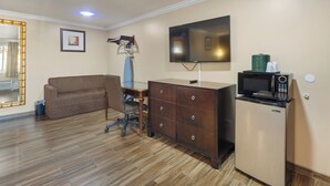 A compact living space with a sofa, a desk, a dresser, a television, and a microwave. - Sky Palm Motel (Orange)