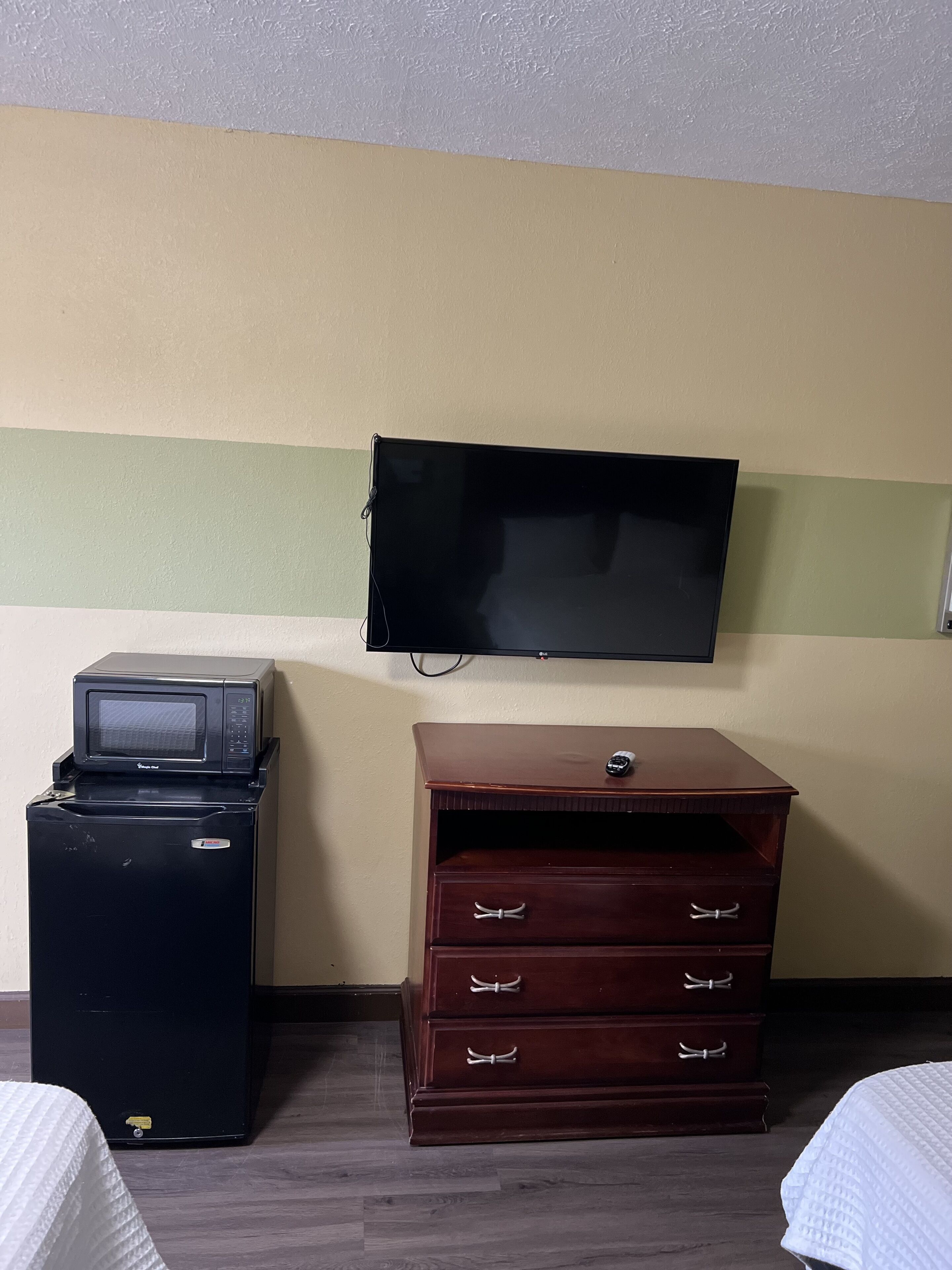 Ein Hotelzimmer mit einem flachbildfernseher an der Wand, einem kleinen Kühlschrank und einer Holzkommode mit Schubladen.