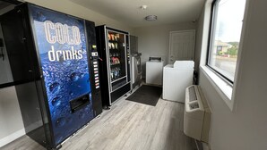 Une pièce équipée d’un distributeur automatique de boissons fraîches, d’un lave-linge et d’un sèche-linge.