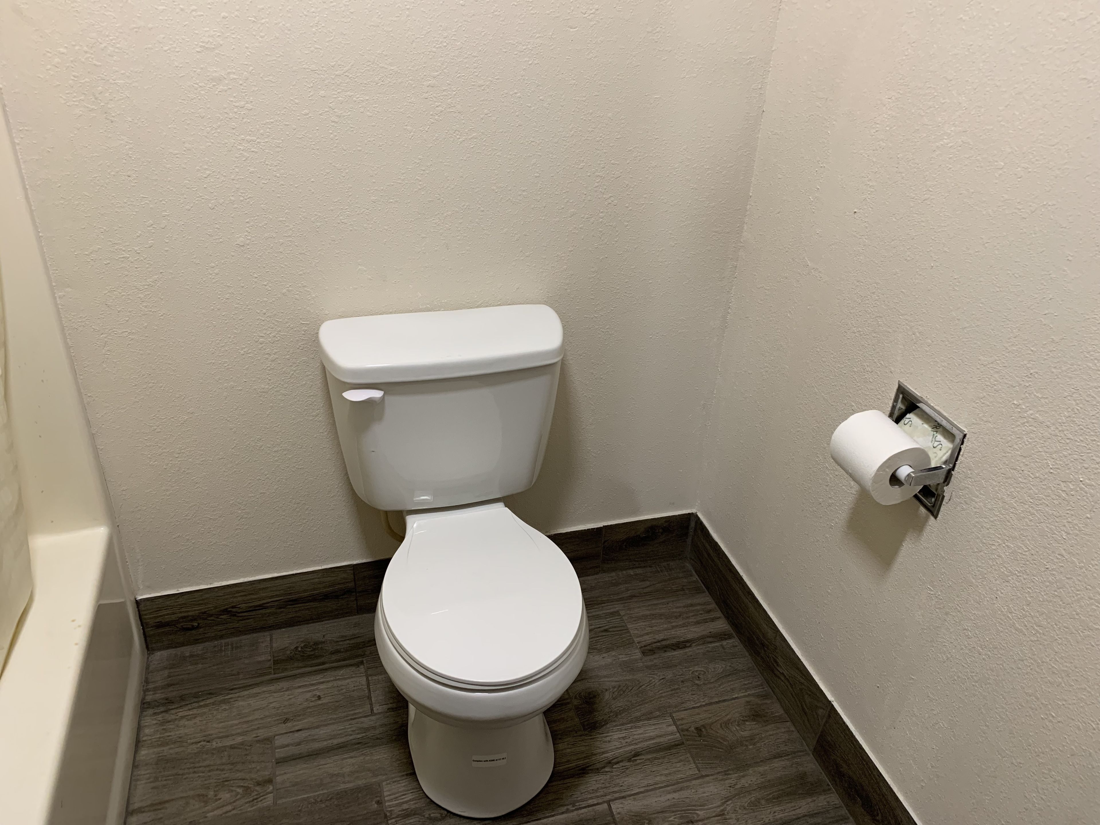 A white toilet with a paper towel holder on the wall.
