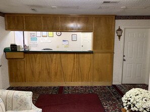 A reception area with a wooden counter, a clock, and various notices on the wall.