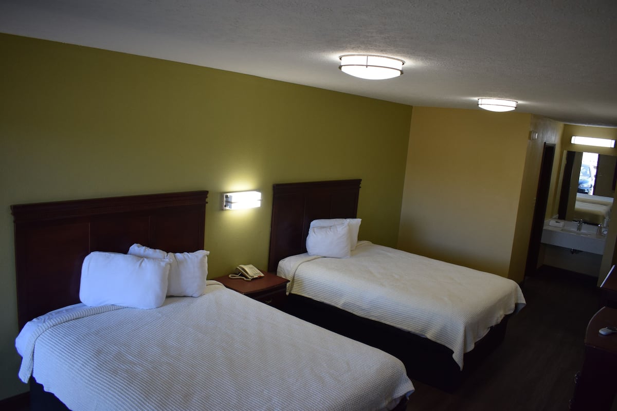Ein Hotelzimmer mit zwei Betten, einem Nachttisch mit Telefon und einem durchgehenden Türbogen einsehbarer Badezimmers.