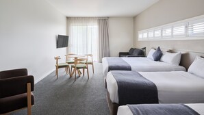 A hotel room with two beds, a TV mounted on the wall, a desk with chairs, and a window with blinds. - Abode Gungahlin (Gungahlin)