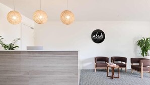 A reception area with a modern reception desk, three hanging pendant lights, and a sign reading "abode apartment hotels". - Abode Gungahlin (Gungahlin)