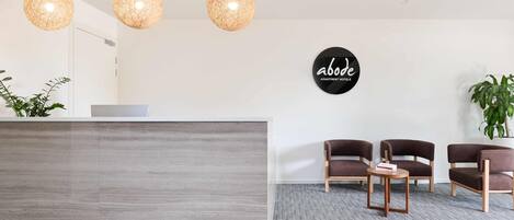 A reception area with a modern reception desk, three hanging pendant lights, and a sign reading "abode apartment hotels".