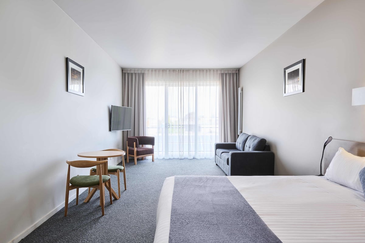 Habitación de hotel con una cama grande, un sofá, un televisor y un escritorio con sillas.