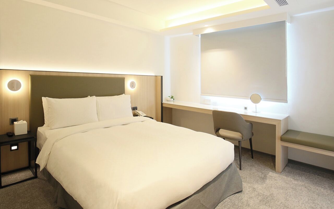 A hotel room with a large bed, a desk with a chair, and a window.