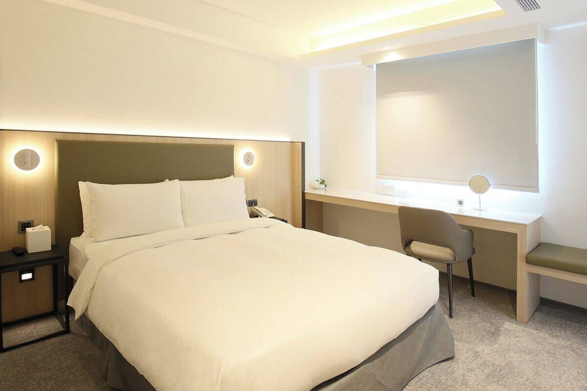 Quarto de hotel com uma cama grande, uma mesa com cadeira e uma janela.