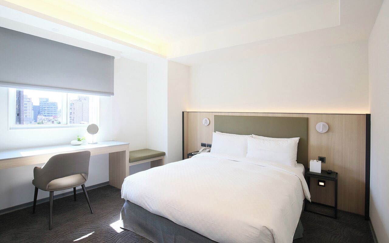 A hotel room with a large bed, a desk, and a chair.
