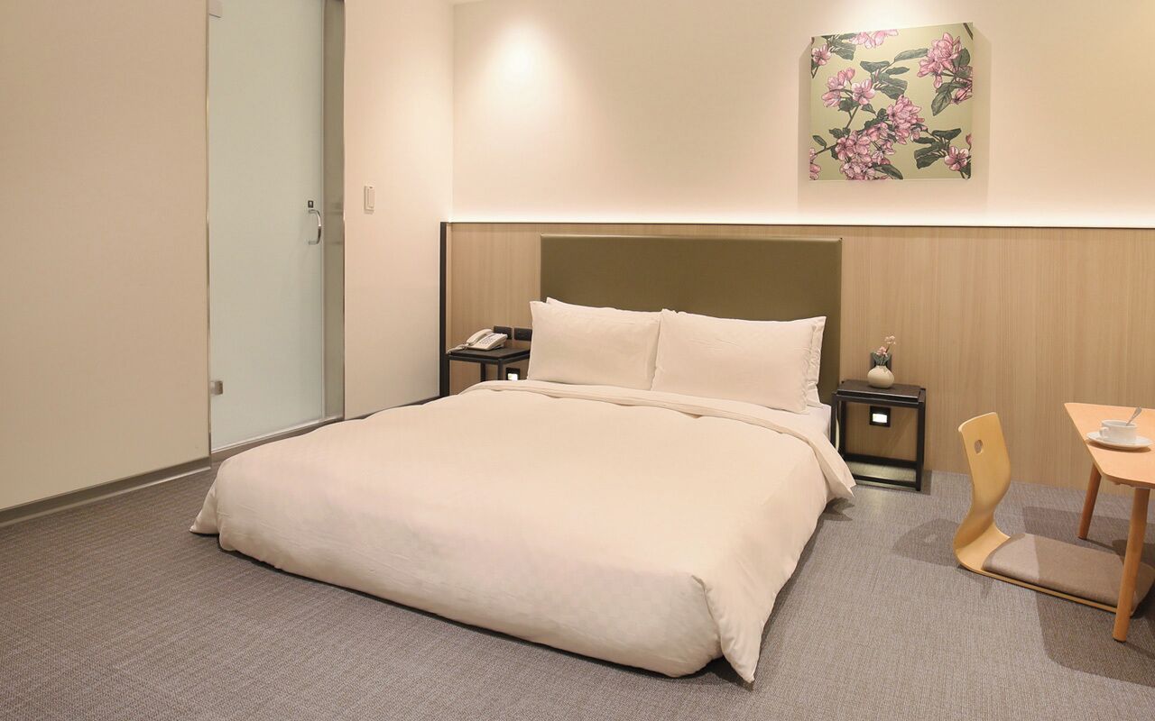 Ein Hotelzimmer mit einem großen Bett, Nachttischen, einem Sessel und einem kleinen Tisch.