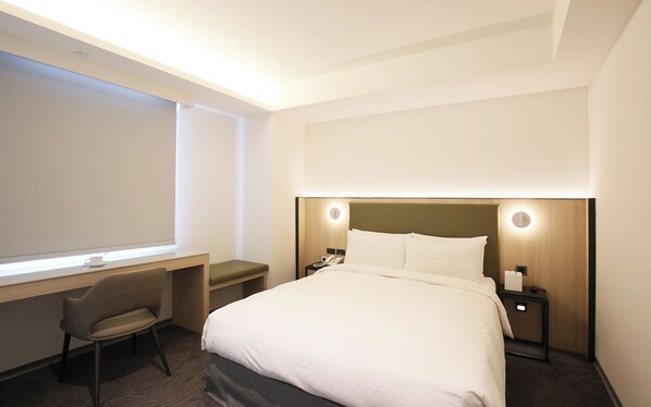 Habitación de hotel con una cama, un escritorio, una silla y una mesita de noche con un teléfono.