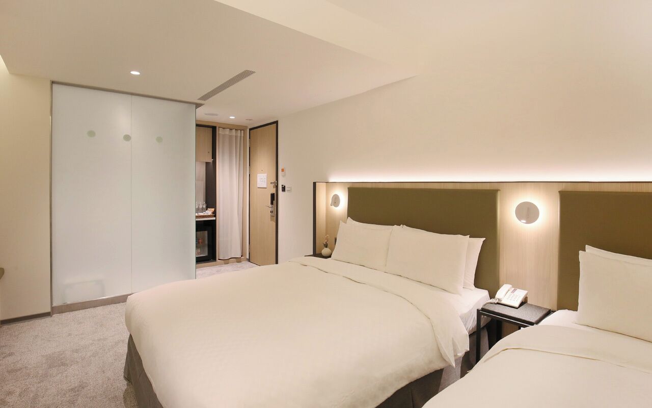 A hotel room with a large bed, a bedside table with a phone, and a door leading to a bathroom.