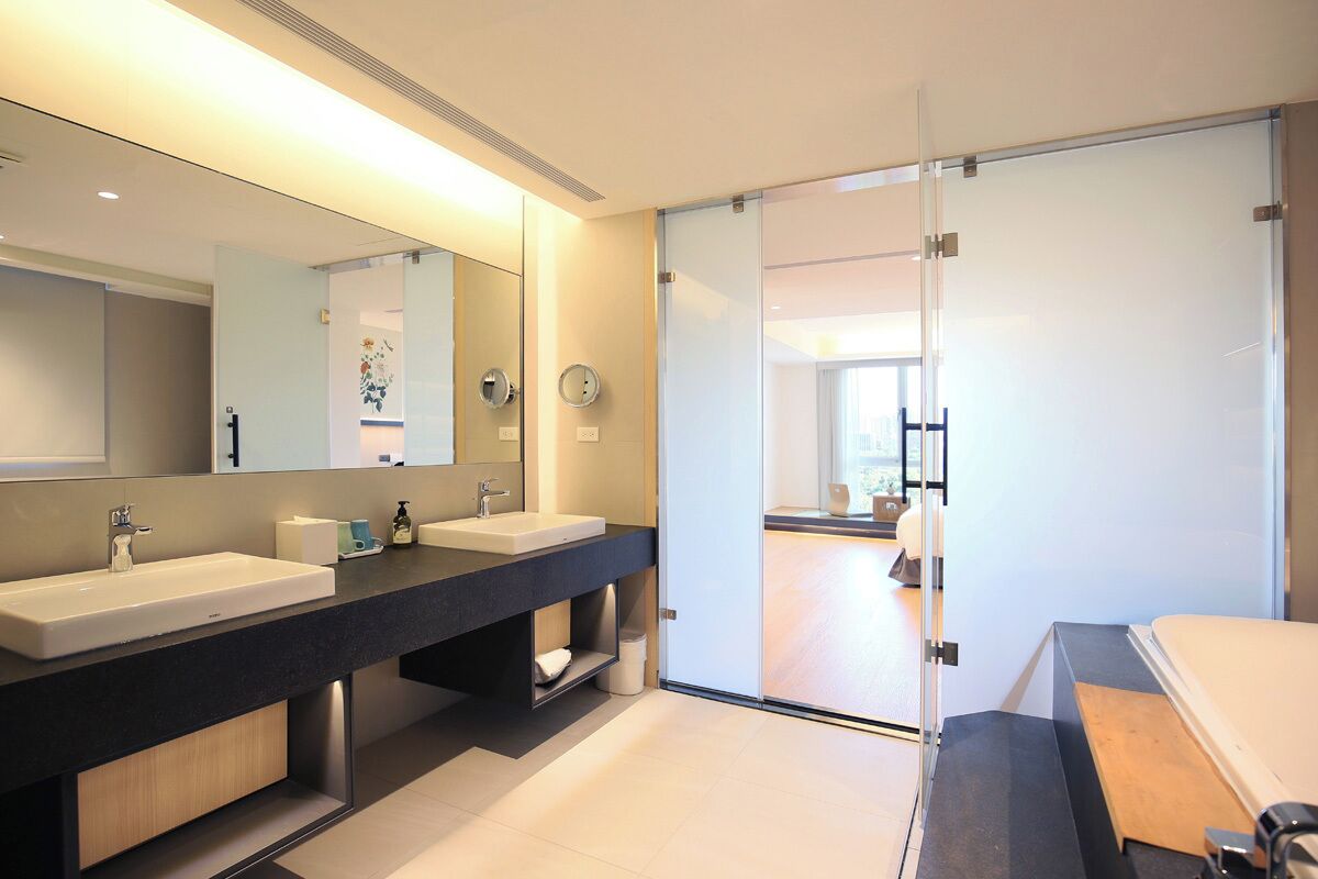 A modern bathroom with two sinks, a large mirror, and a sliding glass door leading to a bedroom.