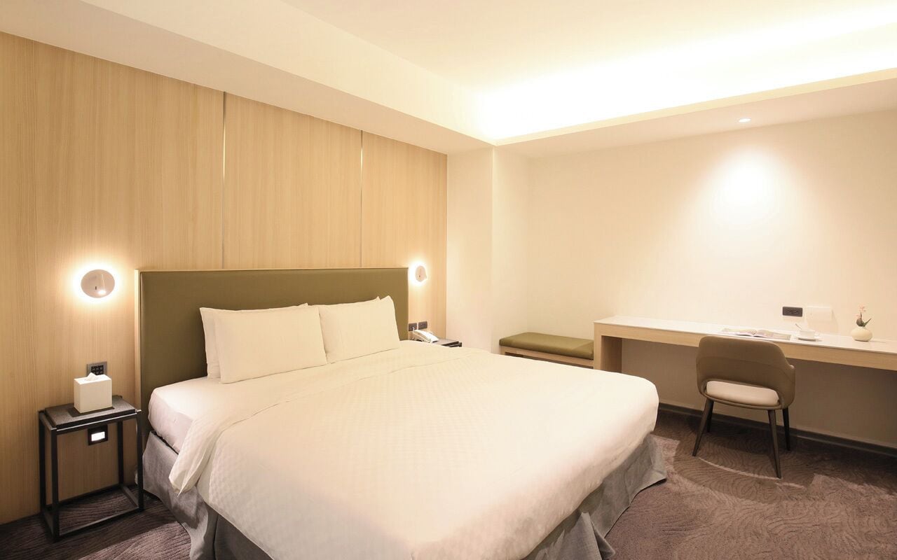Hotellihuoneessa on suuri sänky, työpöytä ja tuoli. Huoneessa on myös yöpöytä, jossa on lamppu ja puhelin.